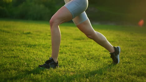The-woman-one-jumps-out-and-changes-her-legs-in-turn-by-training-the-thighs-and-buttocks.-Womans-training-in-the-park-at-sunset